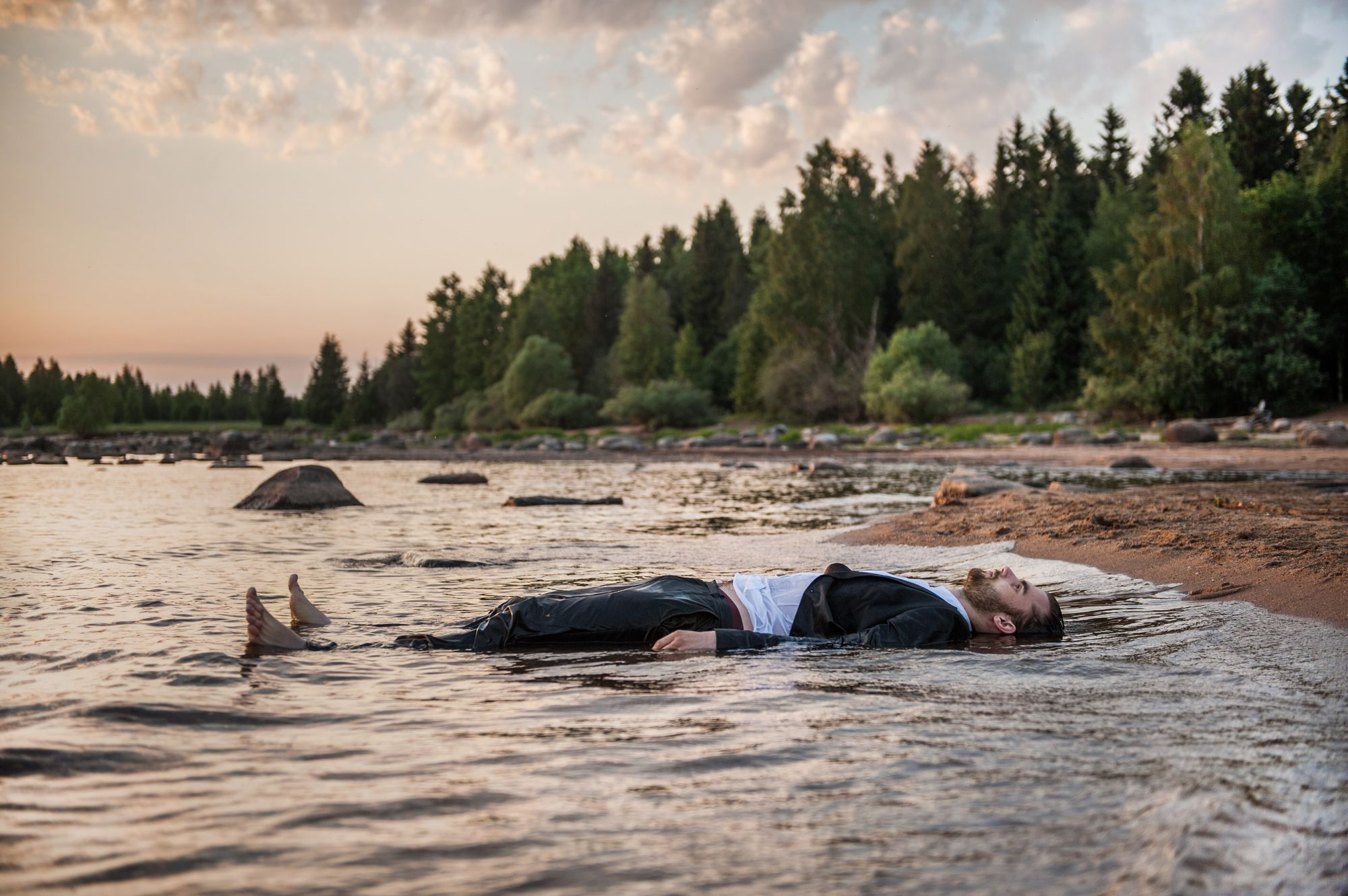 Man in clothes lying in shallow water at the edge of a reservoir