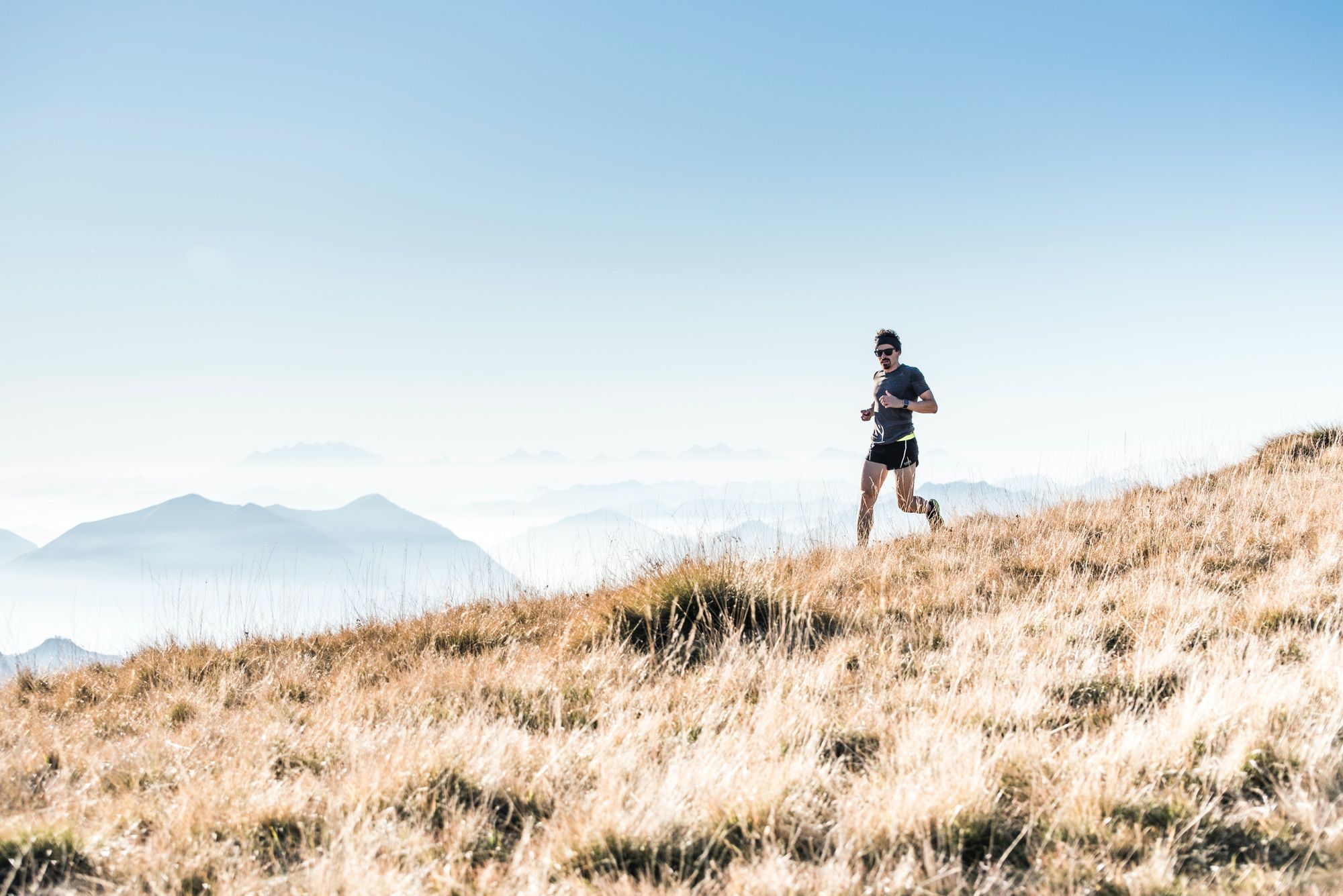 Male trail runner running across high grassland with misty mountains in the distance
