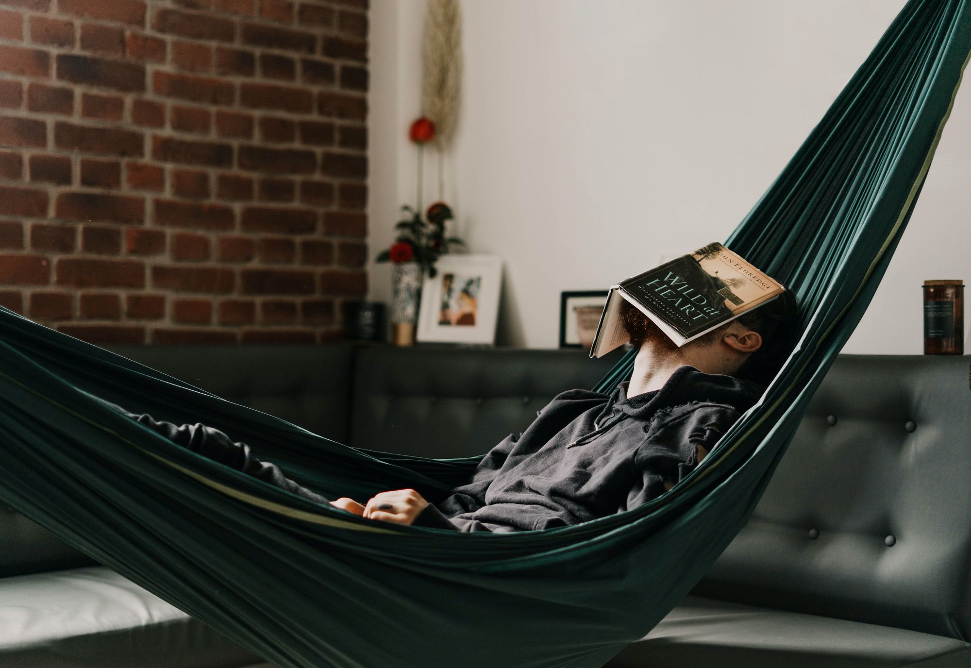 Man lying in an indoor hammock with a book over his face
