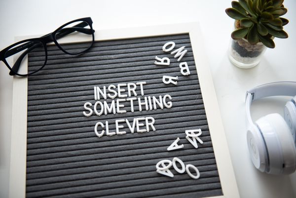 Picture of some glasses, headphones and a plant on a desk. Letters are arranged to say "Insert Something Clever"
