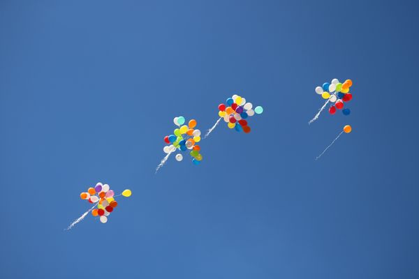 A few bunches of balloons floating into a bright blue sky
