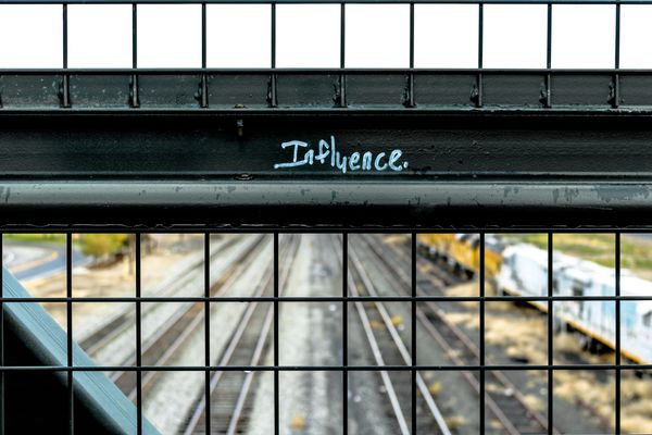 The word "influence" graffitied onto a metal bridge above railway lines